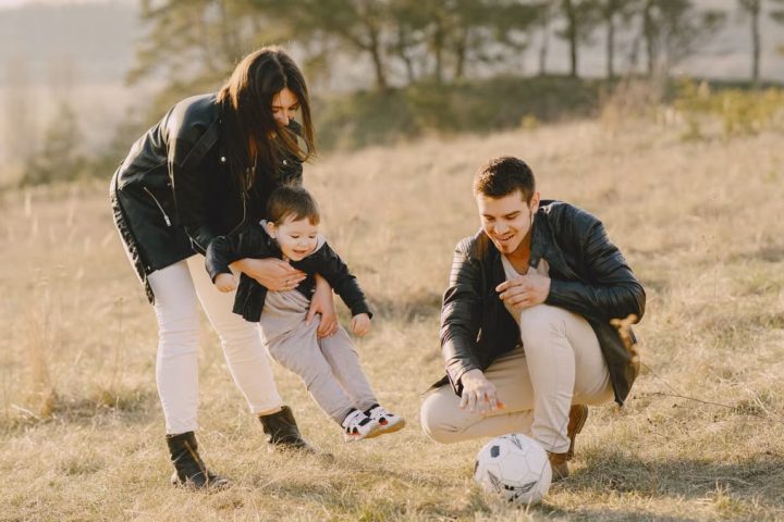 A happy family playing with a soccer ball in a grassy field on a sunny day.
